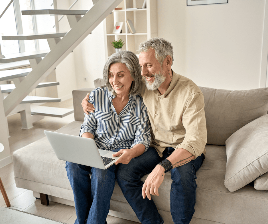 Couple enjoying a joyful moment on a sofa, engaged with a laptop in a bright, modern living space.