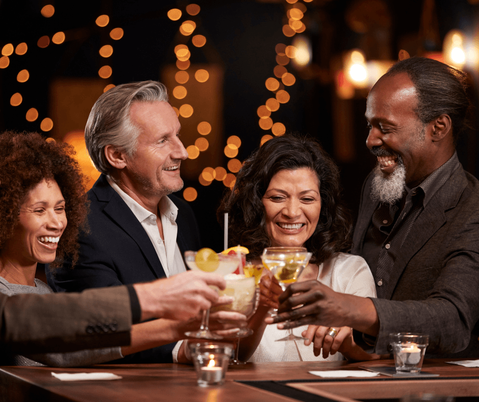 A diverse group of four friends joyfully toasting with cocktails in a warmly lit, upscale bar setting.