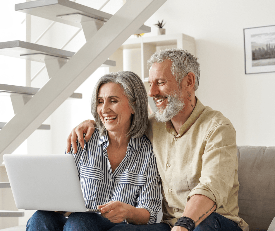 Couple joyfully sharing a moment together, smiling while using a laptop in a bright, modern living space.