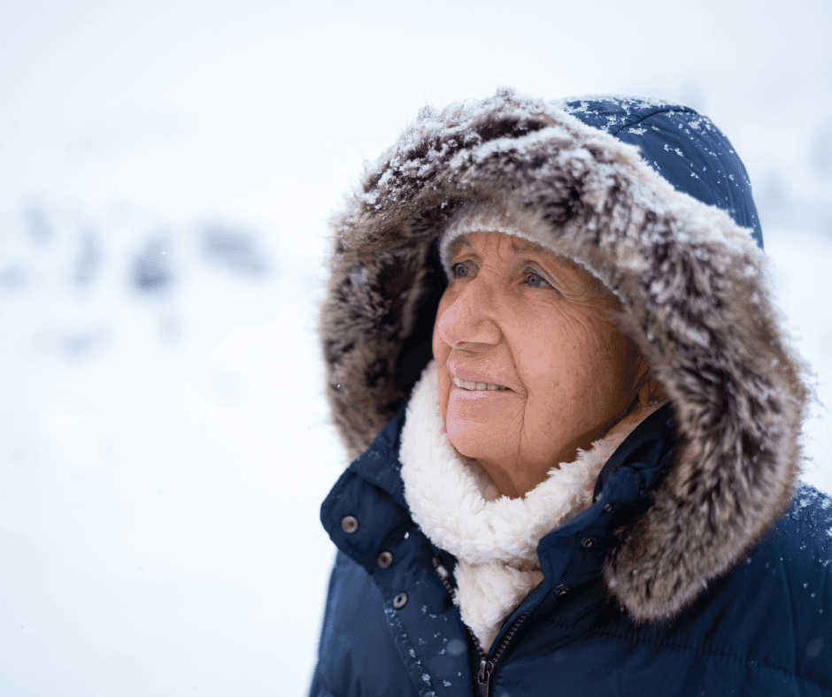 Smiling senior woman in a warm coat with a fur hood, enjoying a serene snowy landscape.