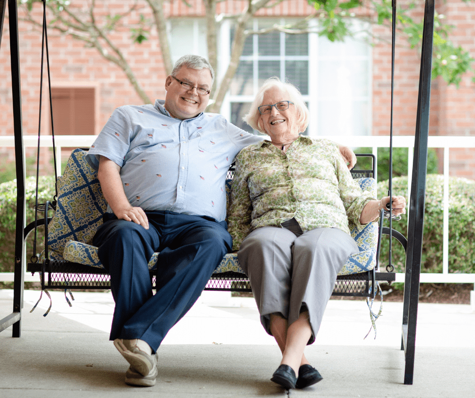 Joyful seniors sharing a moment on a swing, surrounded by vibrant greenery and a welcoming atmosphere.