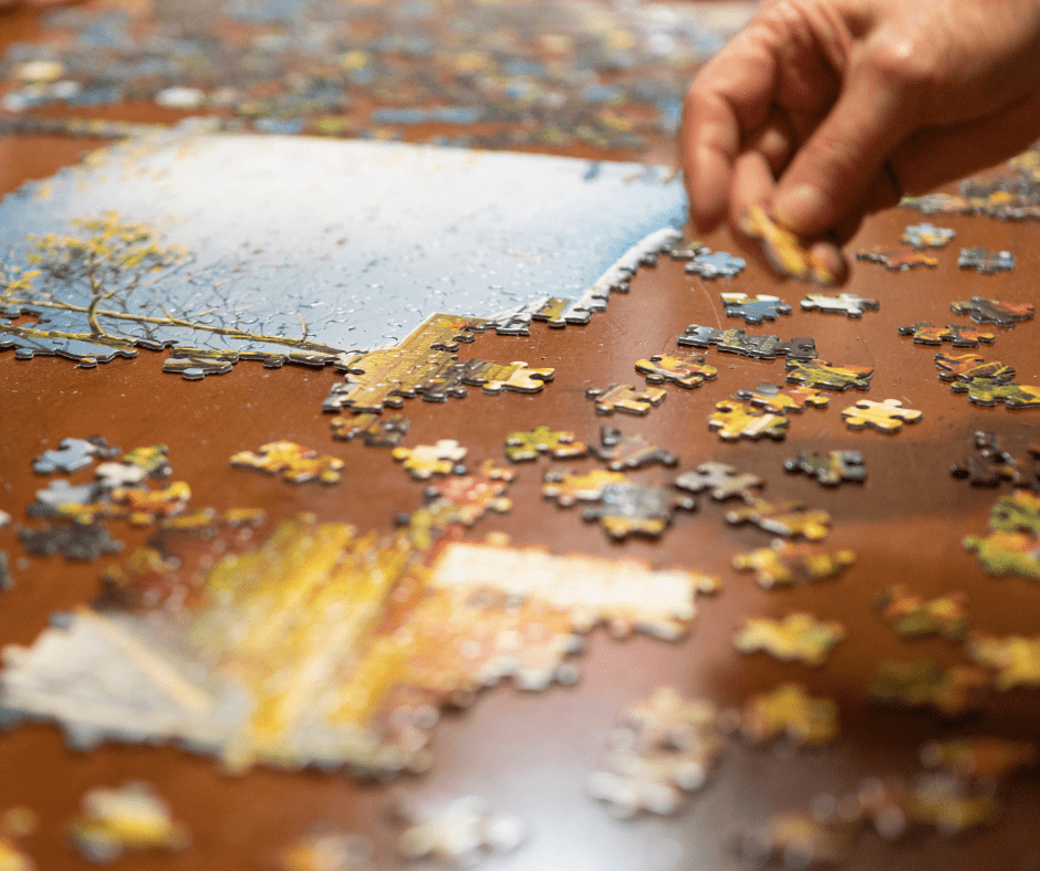 A hand picks up a puzzle piece, surrounded by colorful pieces on a table, fostering engagement and connection.