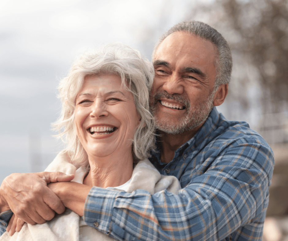 Joyful elderly couple embracing outdoors, sharing laughter and warmth against a serene, blurred backdrop.