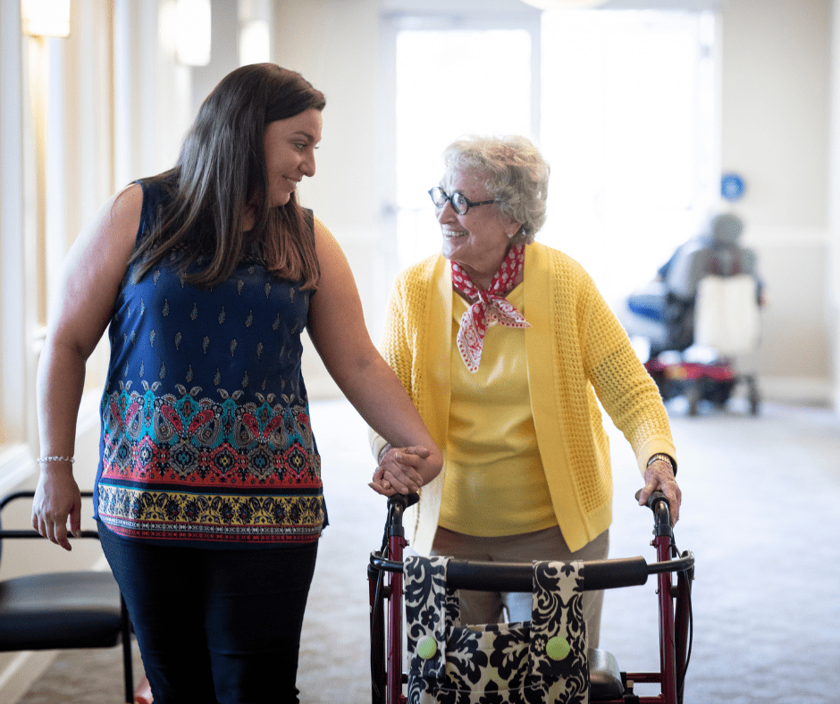 Caregiver and senior woman share a joyful moment while walking in an upscale setting, showcasing compassionate support.
