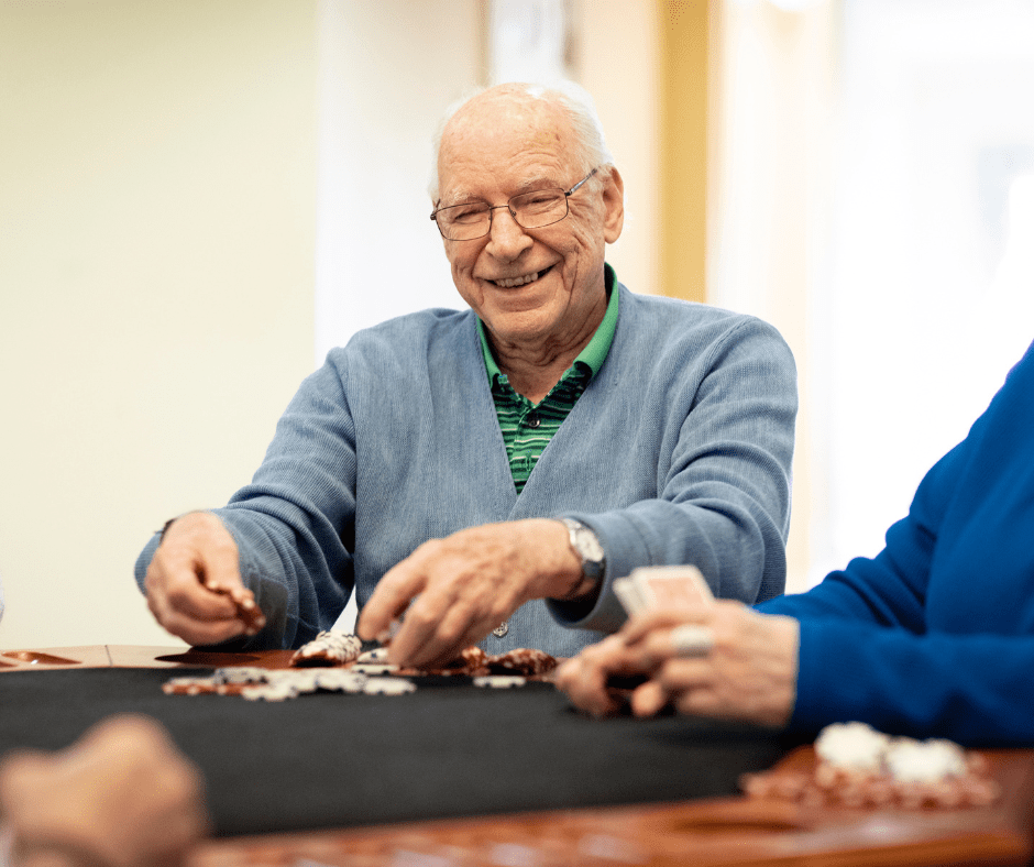 Senior man happily playing cards with friends, engaged in a vibrant social activity in a cozy, welcoming setting.