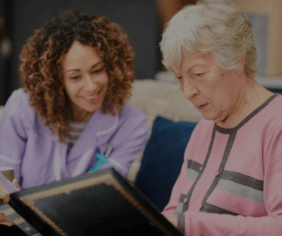 Compassionate caregiver engaging with an elderly resident, sharing moments over a scrapbook in a cozy living space.