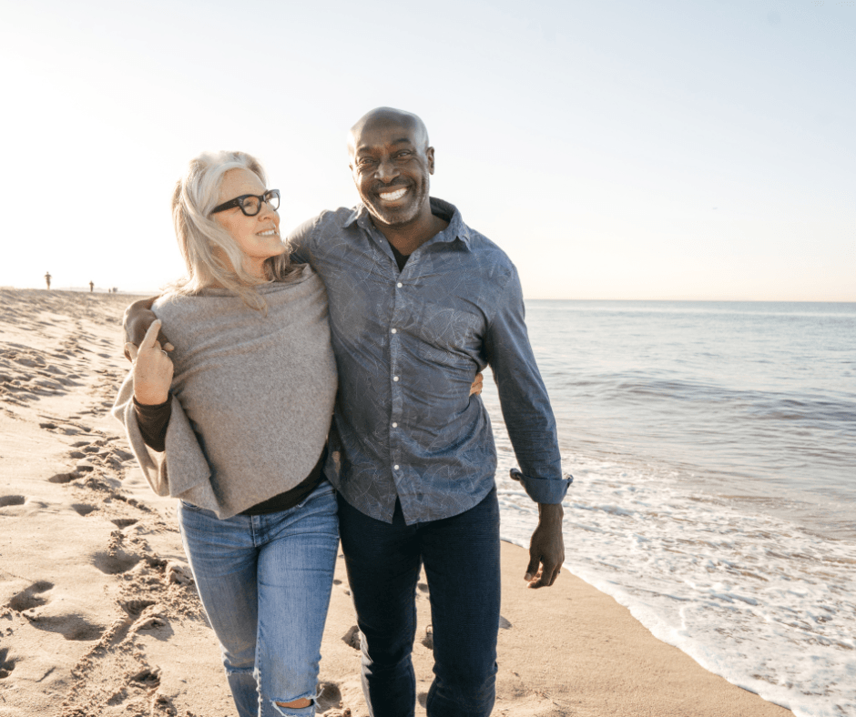 Couple joyfully walking along a sunny beach, embracing a vibrant lifestyle and connection by the ocean.