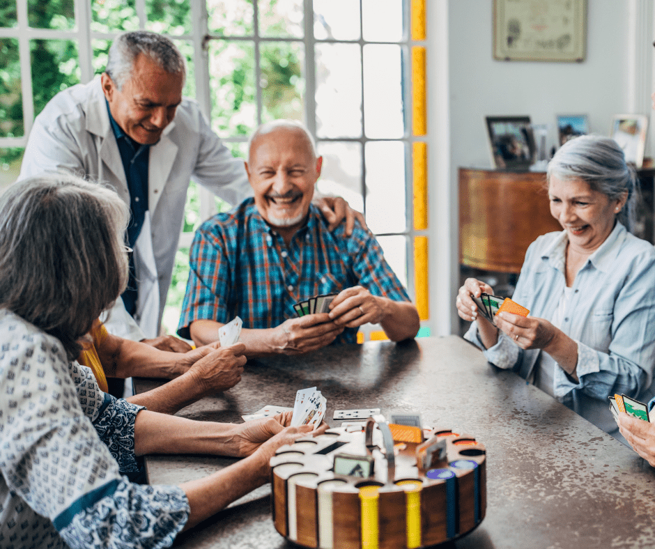 Seniors enjoying a lively card game with a compassionate caregiver in an inviting, sunlit communal space.