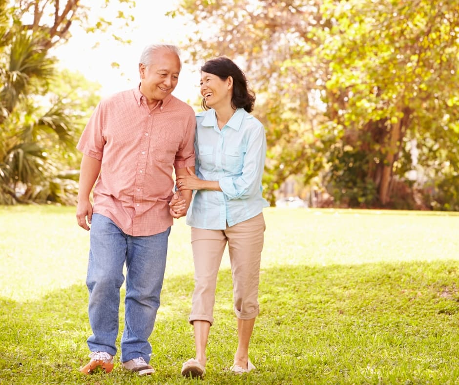 A couple smiles and walks hand-in-hand through a lush green park, enjoying a vibrant outdoor moment together.