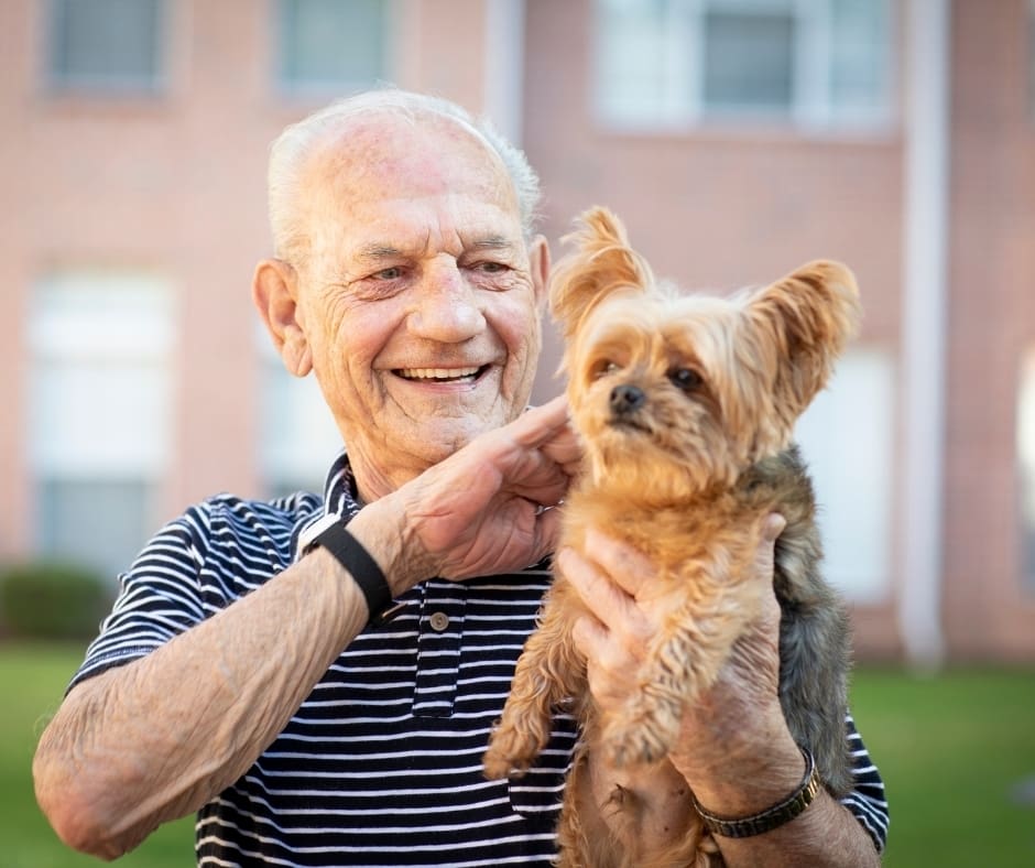 Senior man joyfully holds a small dog outdoors, showcasing a vibrant lifestyle and companionship.
