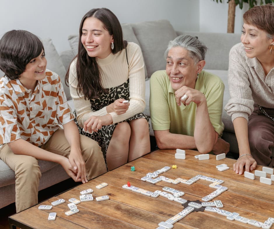 Four generations enjoying a lively game of dominoes in a warm, inviting living room.