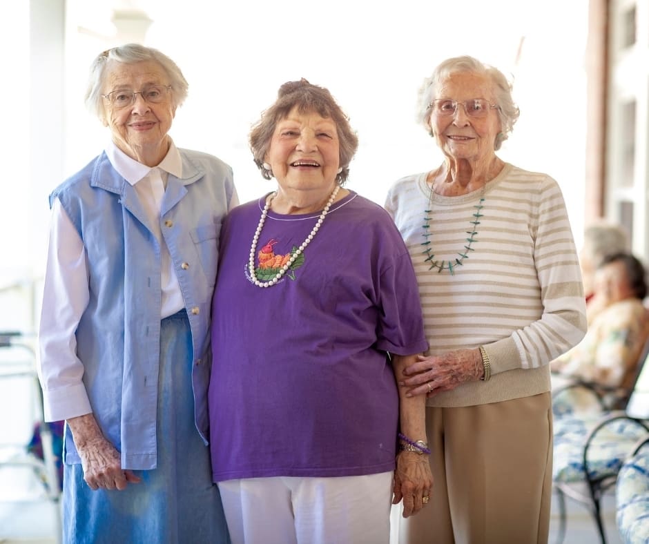 Three smiling senior women pose together, showcasing friendship and joy against a bright, inviting setting.