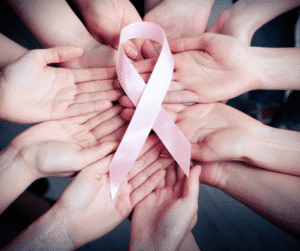 10-4-23 - Grace Management Hands of diverse individuals gather together, holding a pink ribbon symbolizing support for breast cancer awareness.