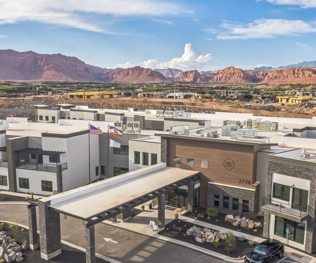 Aerial view of a modern senior living community, featuring upscale amenities and stunning mountain backdrop under a clear sky.