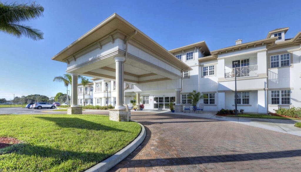 Welcoming entrance of an upscale senior living community with lush landscaping and elegant architecture under a clear blue sky.