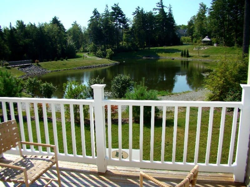Scenic view from a balcony overlooking a serene pond surrounded by lush greenery and gentle hills.