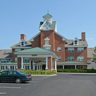 Upscale senior living community with elegant architecture, lush landscaping, and ample parking under a clear blue sky.