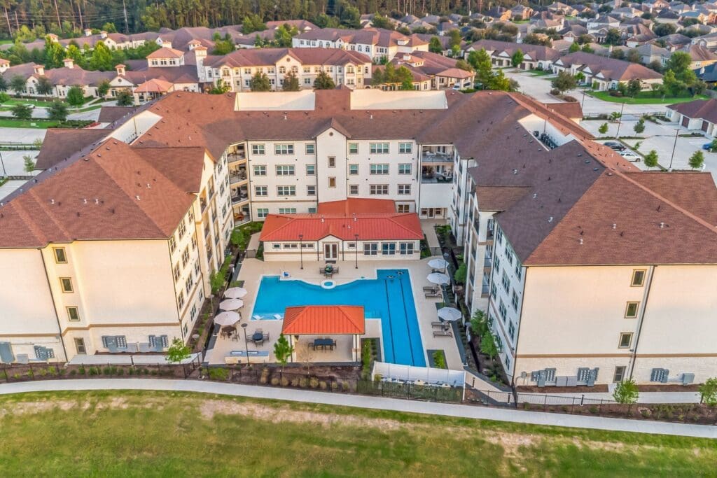Aerial view of an upscale senior living community featuring elegant buildings, a pool, and landscaped outdoor spaces.
