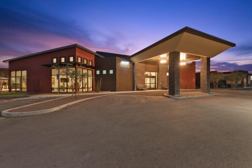 Modern senior living facility exterior with elegant architecture, inviting entrance, and warm twilight sky backdrop.
