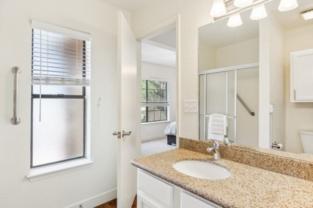 Well-appointed bathroom featuring a granite countertop, stylish mirror, and a glimpse of the serene living space beyond.