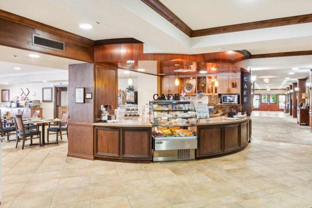 Elegant café area featuring a pastry display, warm wooden décor, and inviting dining arrangements for a vibrant community.