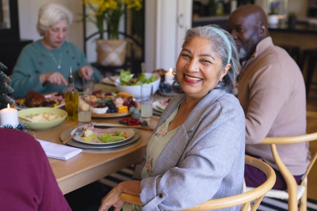 Cheerful woman smiles at a festive dining table filled with delicious food, surrounded by engaged companions in an inviting setting.