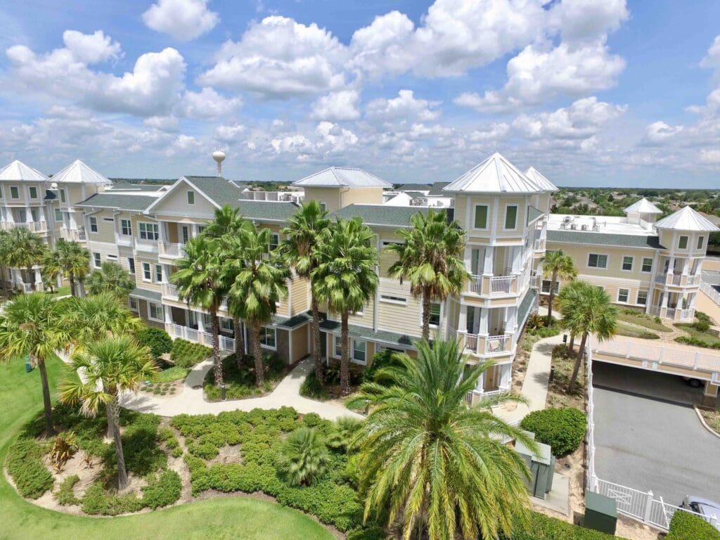 Aerial view of an upscale senior living community surrounded by lush palm trees and vibrant landscaping under a sunny sky.