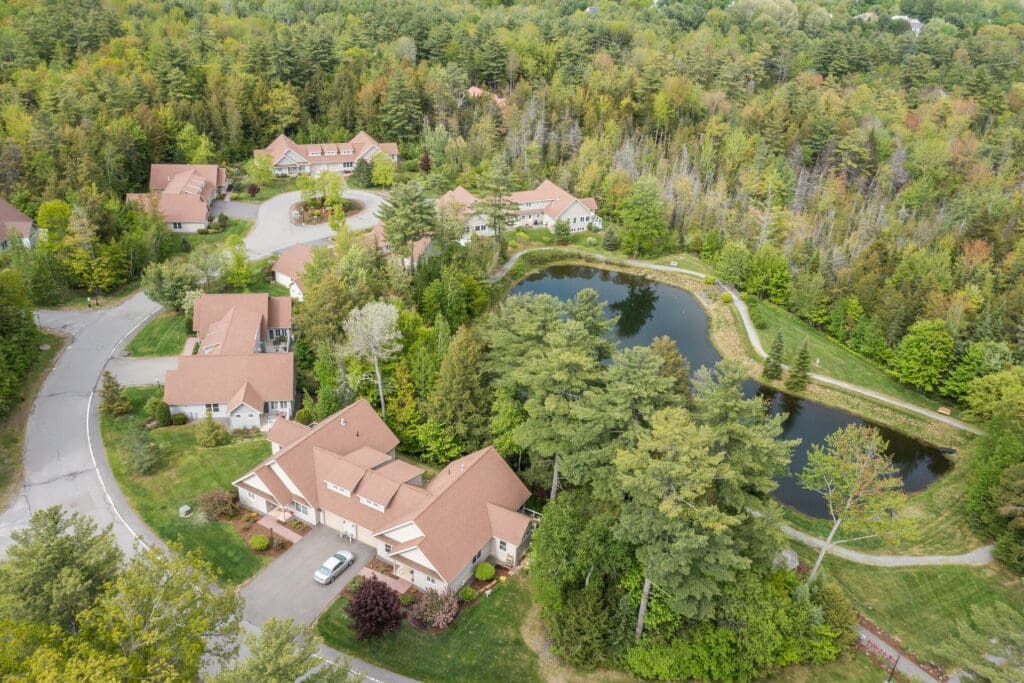 Aerial view of a vibrant senior living community surrounded by lush greenery and a serene pond, showcasing upscale residences.
