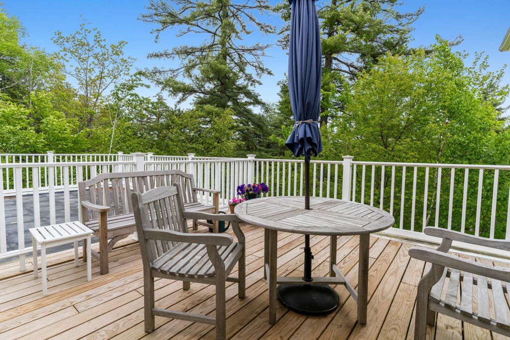Outdoor patio featuring elegant wooden furniture and a vibrant umbrella, surrounded by lush greenery and serene views.