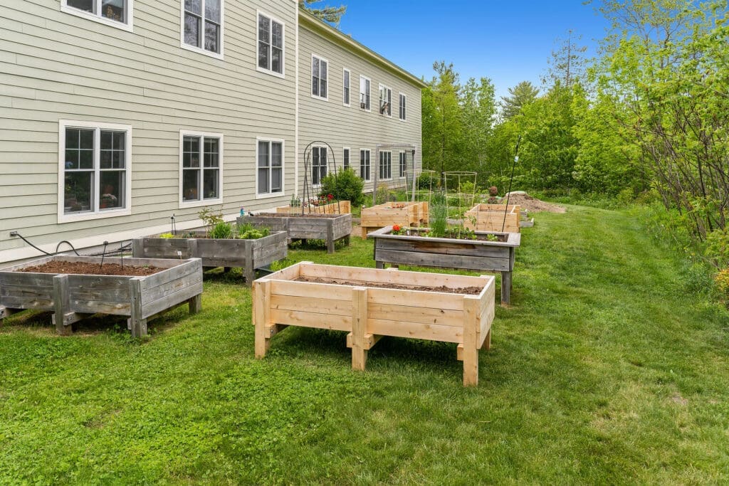 Lush community garden featuring raised beds and vibrant greenery, located beside an elegant senior living residence.