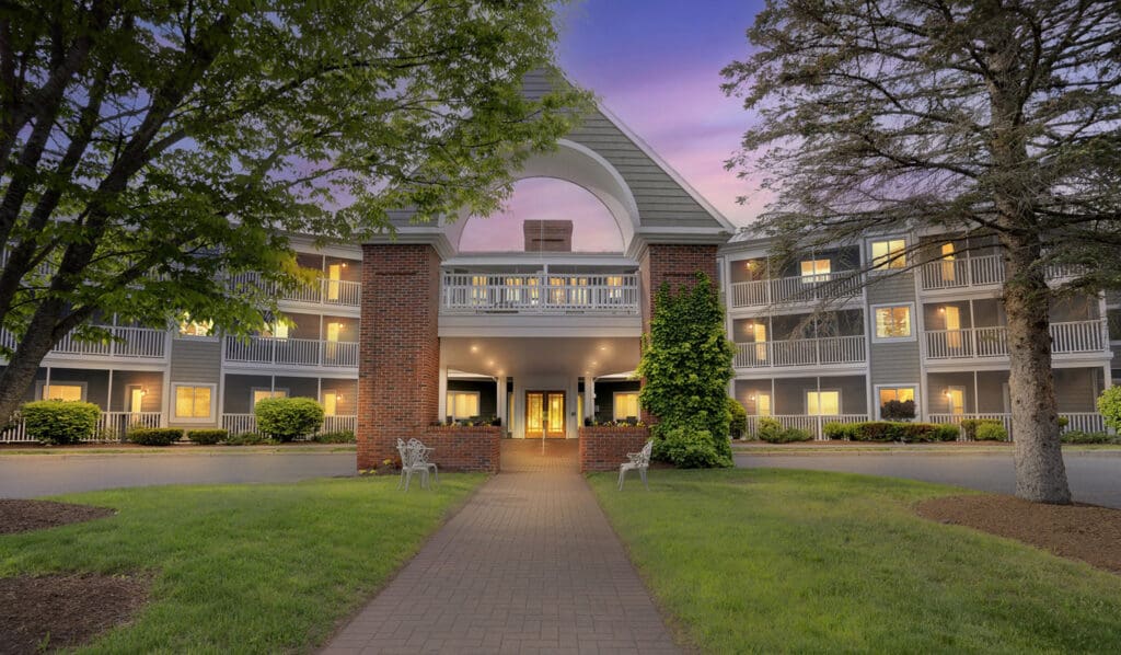 Inviting entrance of a senior living community, featuring lush greenery, elegant architecture, and warm, welcoming lights.