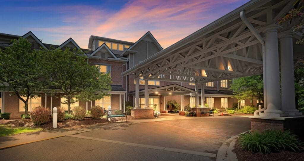 Beautiful entrance of an upscale senior living community, featuring elegant architecture, lush landscaping, and warm lighting.