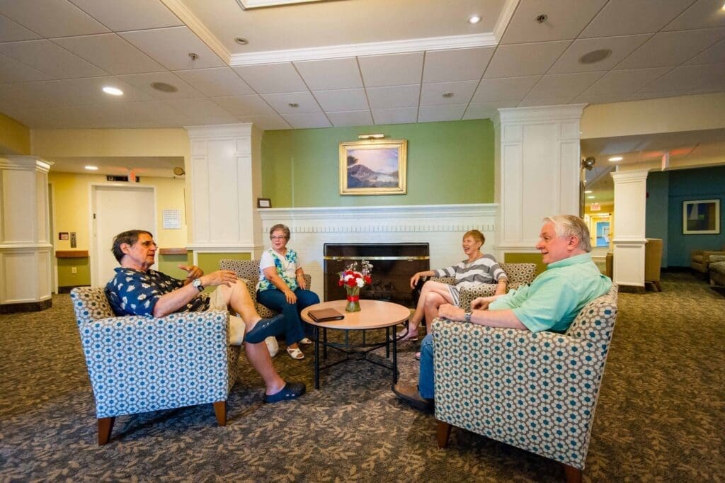 Four seniors engage in lively conversation in an inviting lobby, surrounded by comfortable seating and warm decor.