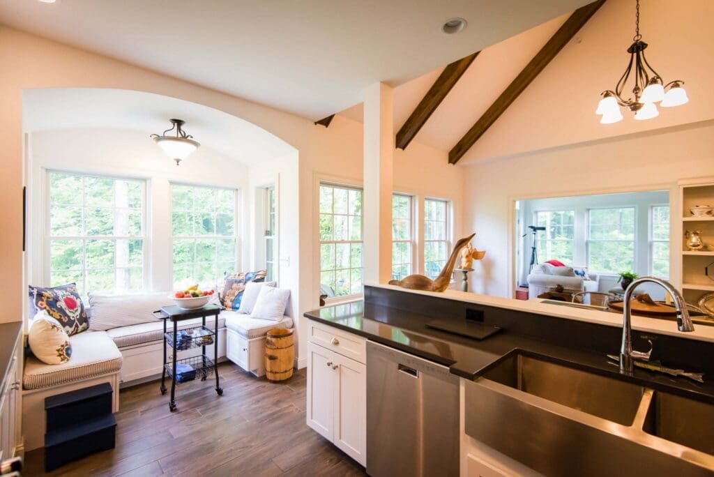 Bright kitchen with modern amenities, cozy seating area by windows, and fresh fruit on a table, showcasing a welcoming ambiance.