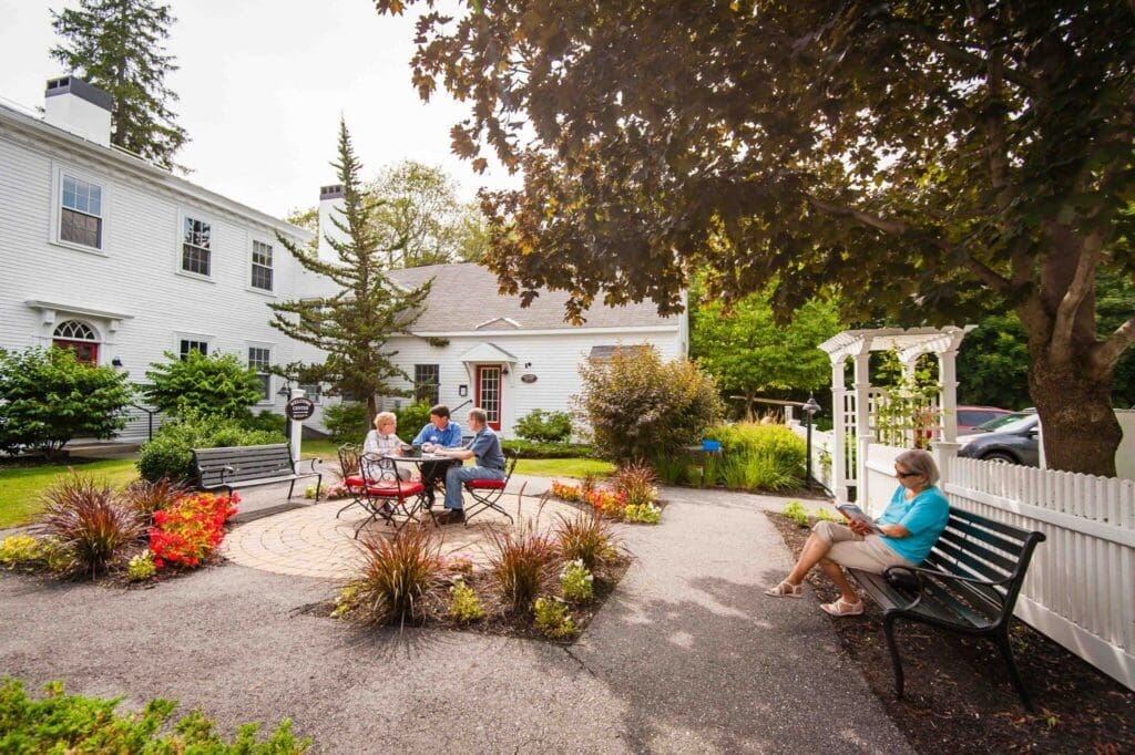 Residents enjoying time outdoors at a senior living community, engaged in conversation and reading in a vibrant garden.