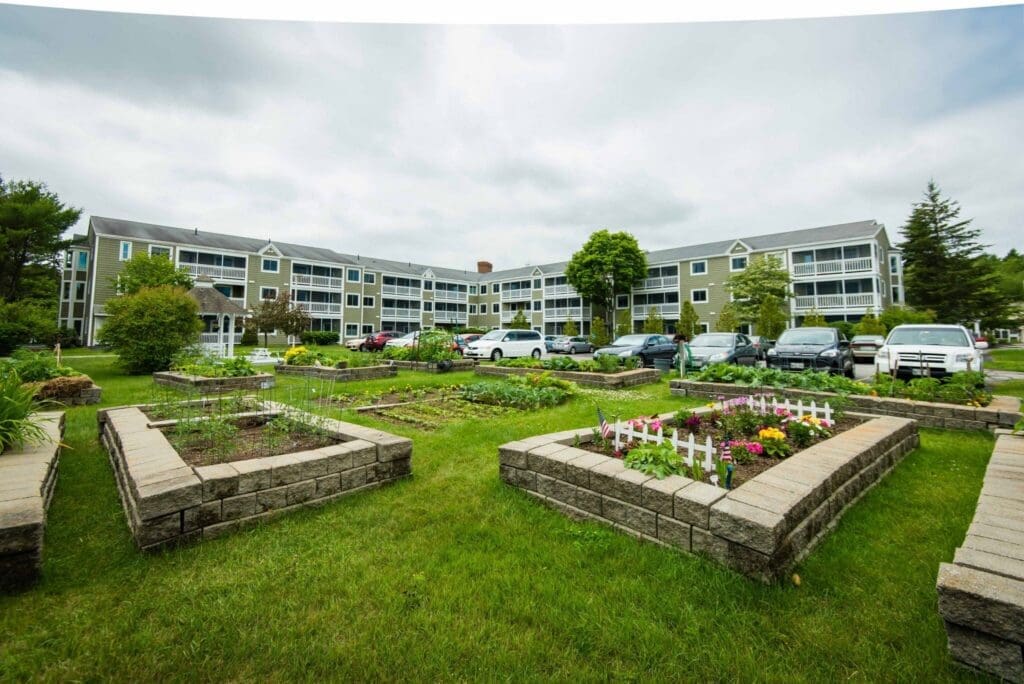 Vibrant senior living community with beautifully landscaped gardens and upscale residential buildings under a cloudy sky.