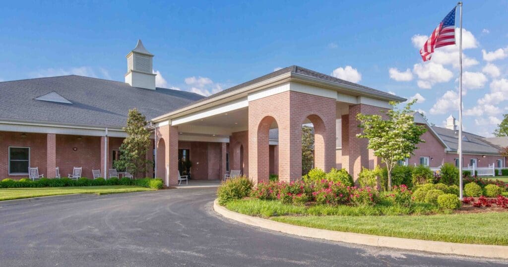 Elegant senior living community entrance featuring well-maintained gardens, welcoming porches, and an American flag.