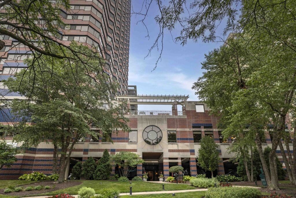 Elegant senior living community entrance surrounded by lush greenery and upscale architecture under a serene blue sky.