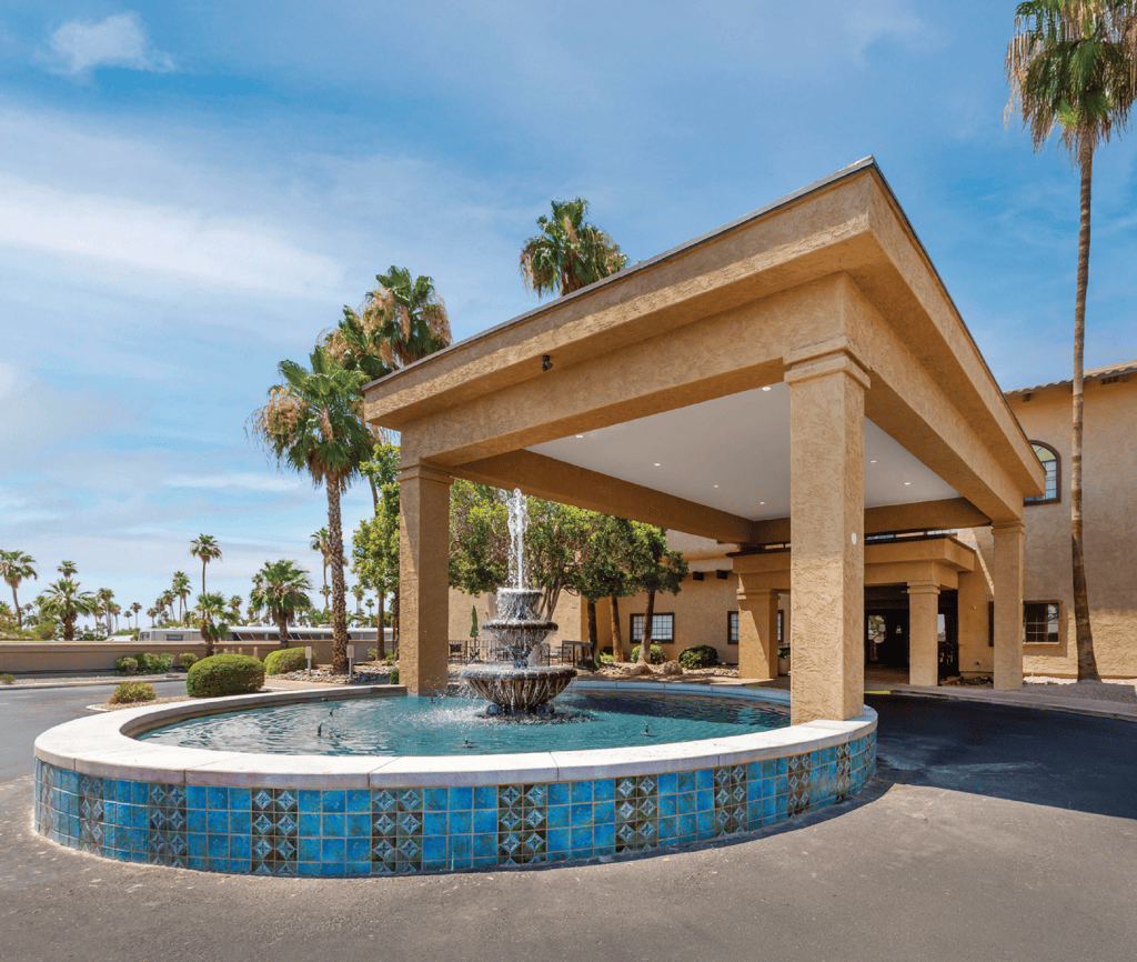 Fountain_InspirationsofMesa - Grace Management Welcoming entrance featuring a decorative fountain, lush palm trees, and upscale architecture under a bright blue sky.