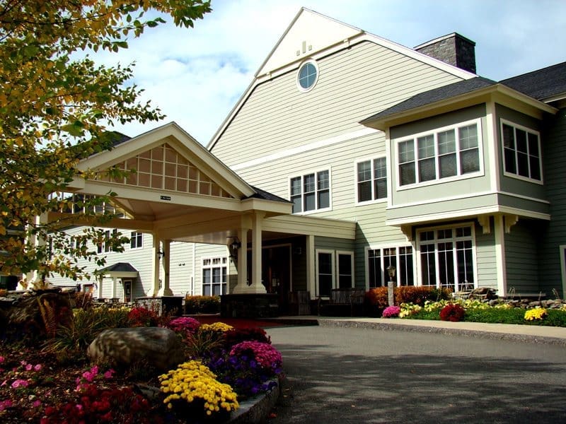 Elegant senior living community entrance with vibrant flowers and welcoming facade under a clear sky.
