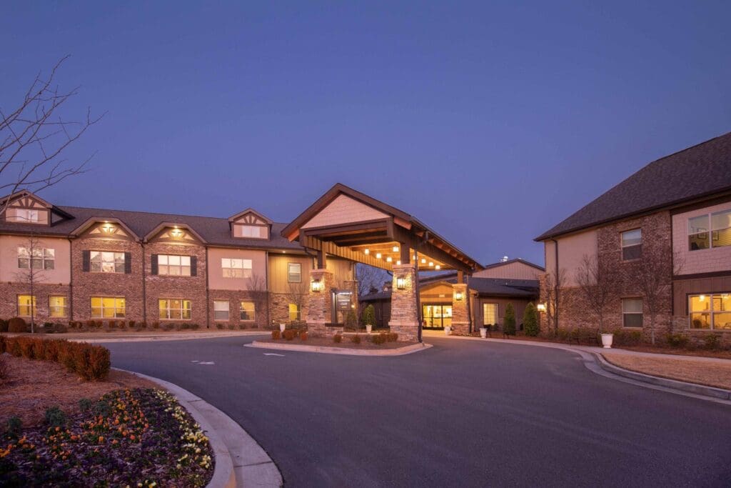 Elegant senior living community entrance at dusk, showcasing warm lighting and beautifully landscaped flower beds.