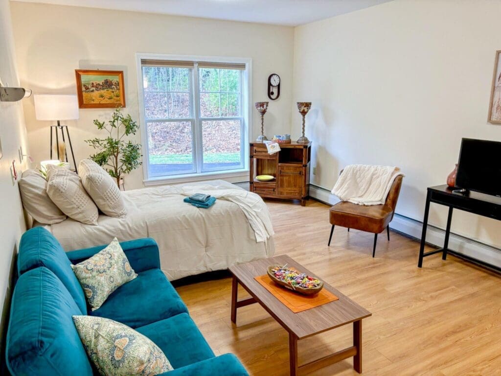 Bright and inviting studio apartment featuring a cozy bed, teal sofa, and warm wood accents for a vibrant lifestyle.
