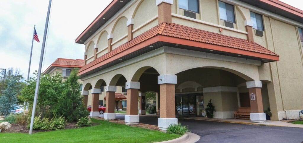 Welcoming entrance of a senior living community featuring stylish architecture, lush greenery, and inviting seating areas.