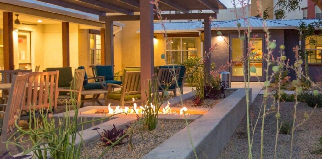Sage-Desert-Tucson-AZ-2018-June-0683-scaled-e1687537485216-2048x1014 - Grace Management Elegant outdoor seating area featuring a fire pit, vibrant greenery, and modern architecture, promoting a vibrant lifestyle.