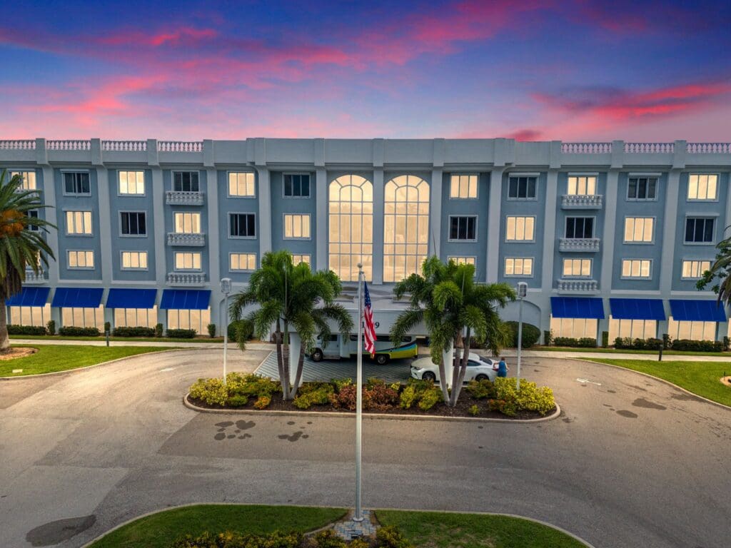 Elegant senior living community with lush landscaping and a welcoming entrance under a vibrant sunset sky.