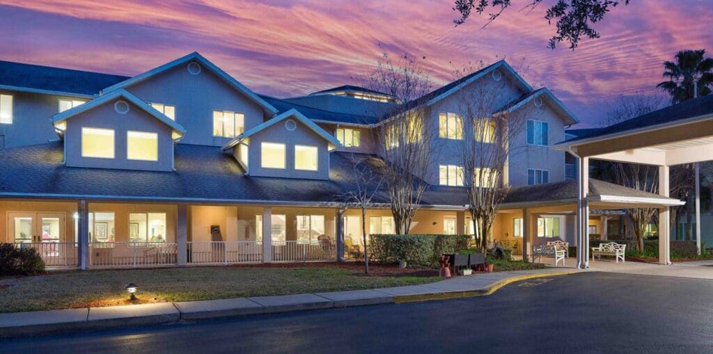 Charming senior living community with welcoming entrance, bright windows, and a picturesque sunset sky.