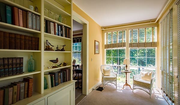 Bright sunlit reading nook with elegant furniture, bookshelves, and a view of nature, creating a serene and inviting atmosphere.