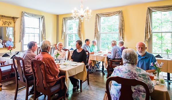 Seniors enjoying a delightful meal in a bright, elegant dining room with floral arrangements and warm lighting.