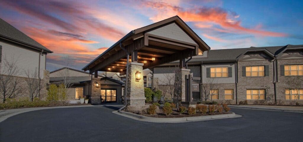 Elegant entrance of a senior living community, featuring upscale architecture and a vibrant sunset sky.