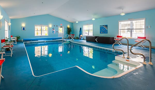 Bright and inviting indoor pool area featuring blue walls, comfortable seating, and easy access for residents.